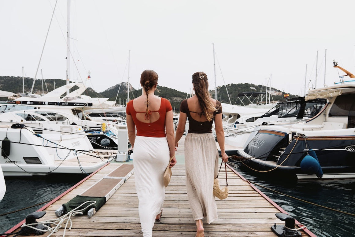 Two women walking along a dock with boats in the background