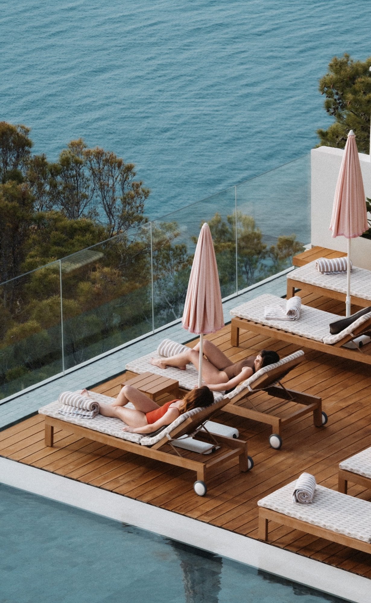 Two people lounging on wooden deck chairs by a pool with ocean view